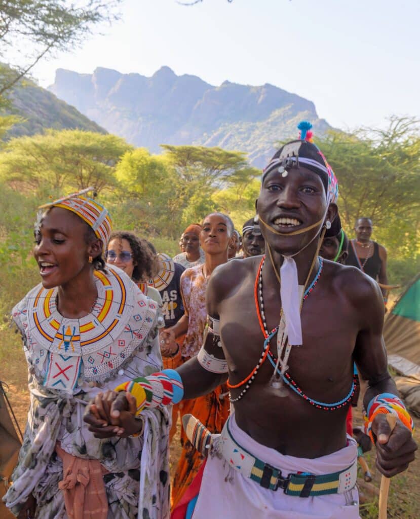 Samburu men and women in ceremonial beadwork singing and dancing hand in hand with participants at camp, below the mountains of northern Kenya